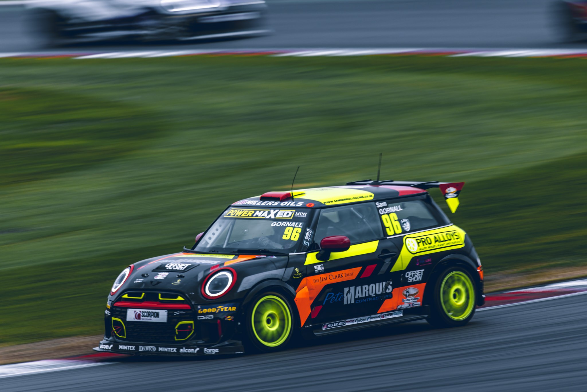 Black and yellow number 96 MINI racing car with bright yellow wheels cornering beside the grass.